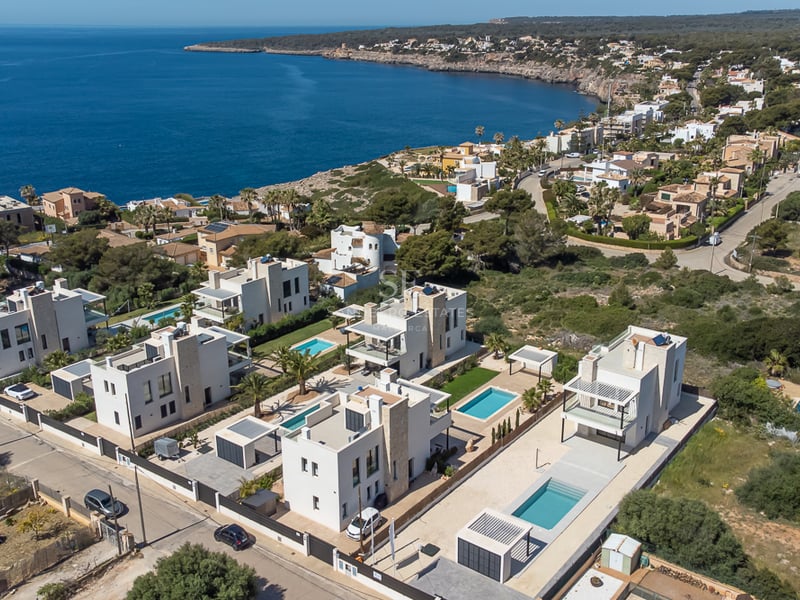 Vue par drone de villas blanches modernes avec piscines privées sur une côte rocheuse au bord de la mer bleue.