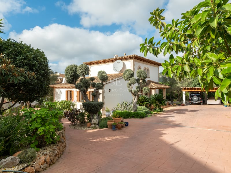 Villa méditerranéenne avec allée en terre cuite, oliviers taillés et parking couvert sous le soleil.