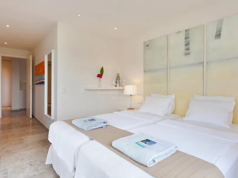 Chambre lumineuse avec lits jumeaux, triptyque artistique, sol en travertin et murs blancs dans une villa moderne.