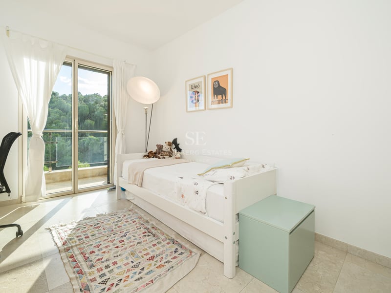 Chambre blanche avec lit simple, bureau, accès terrasse et tapis géométrique.