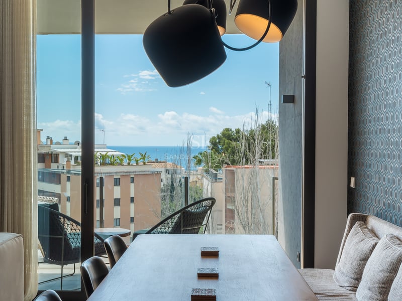 Salle à manger moderne avec table en bois, papier peint bleu et vue panoramique sur la mer Méditerranée.