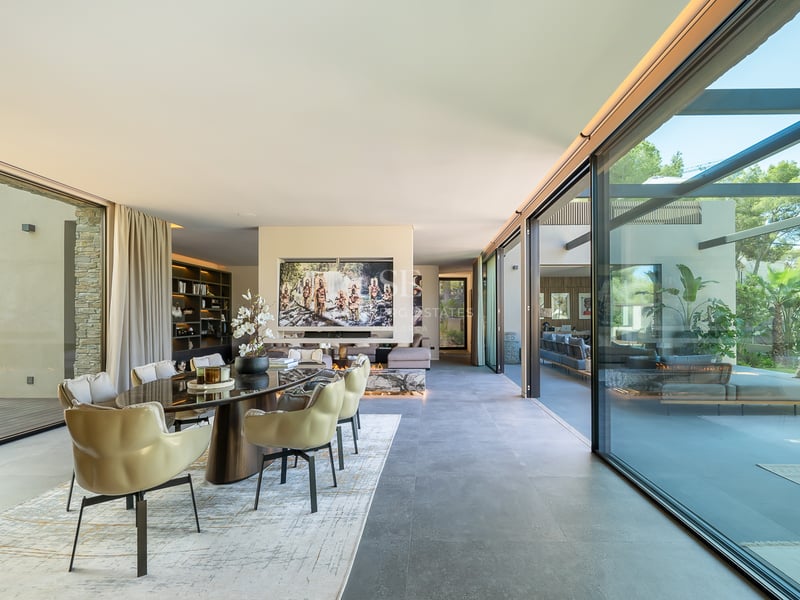 Salle à manger moderne et spacieuse avec baies vitrées, chaises beiges élégantes et vue sur un jardin ensoleillé.