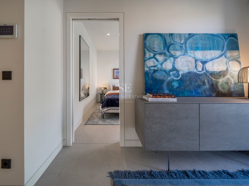 Buffet gris moderne avec peinture abstraite bleue et lampe design, ouvrant sur une chambre lumineuse.