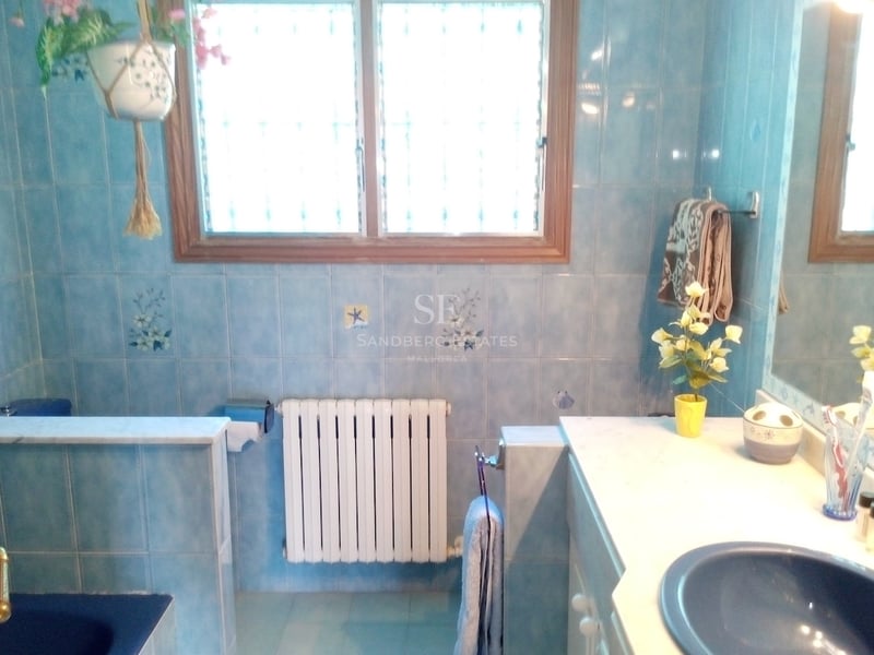 Salle de bain avec carrelage bleu à motifs, plan de toilette en marbre blanc et grande fenêtre.