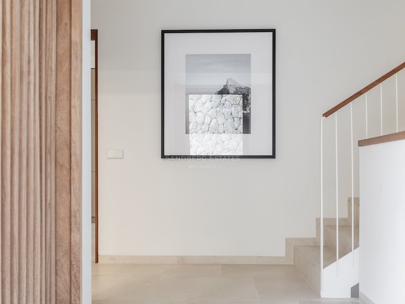 Couloir moderne avec murs blancs, mur en lattes de bois, escalier en pierre et un grand tableau artistique.