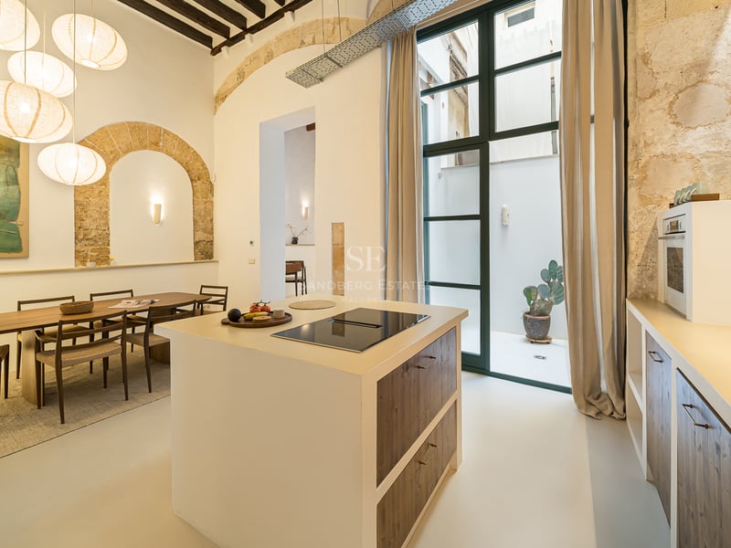 Cuisine moderne avec îlot central, arches en pierre apparente, plafonds en bois et lampes en papier près d'une salle à manger.