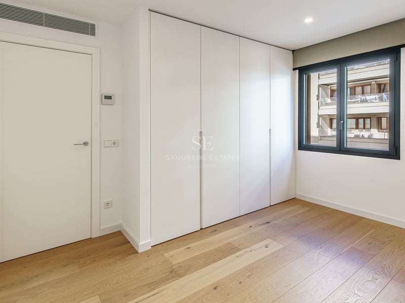 Habitación luminosa con suelos de madera clara, armarios blancos empotrados y ventana con marco oscuro.