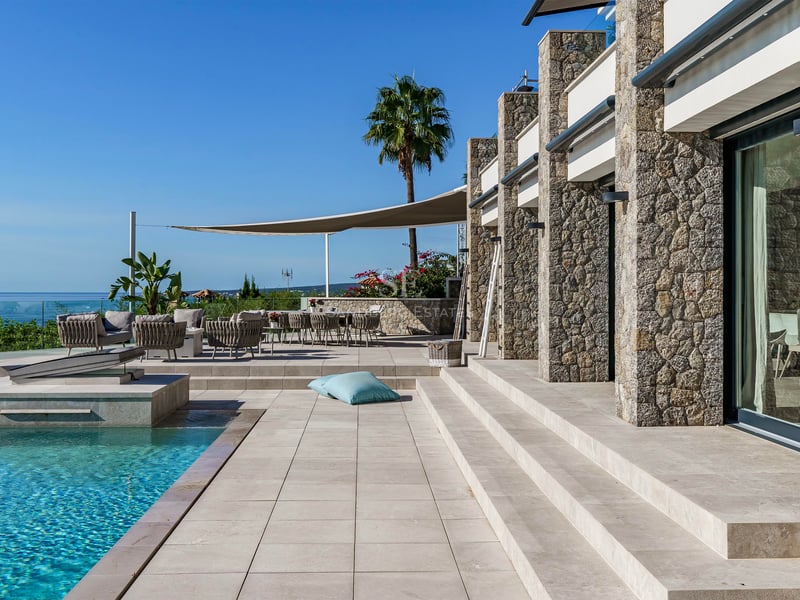 Terrasse en pierre avec piscine à débordement turquoise et salon de jardin face à la mer Méditerranée.