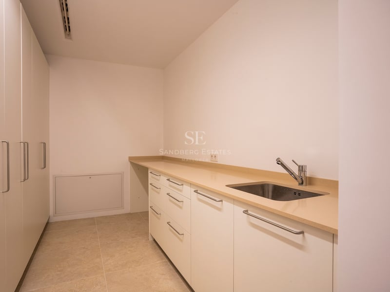 Pièce blanche avec plan de travail beige, évier en inox et grandes armoires de rangement du sol au plafond.