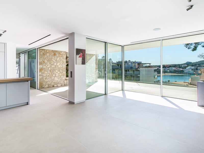 Espace de vie moderne et lumineux avec baies vitrées donnant sur une baie méditerranéenne et mur en pierre.