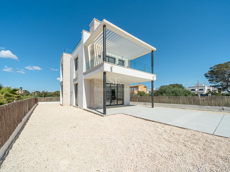 Villa moderne blanche de deux étages avec murs en pierre naturelle, grand balcon et cour en gravier sous un ciel bleu clair.