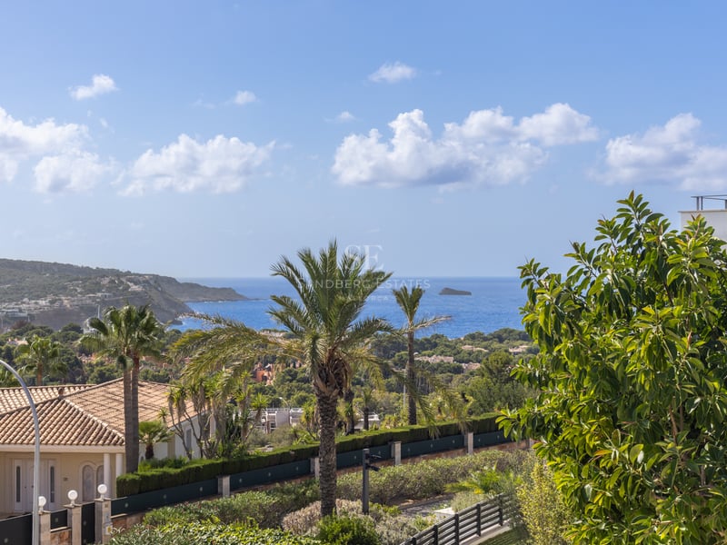 Vue surélevée d'un paysage côtier avec des palmiers, des toits en terre cuite et la mer Méditerranée bleue au loin.