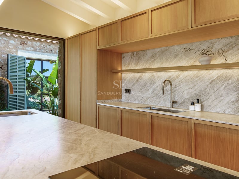 Cocina moderna con muebles de madera clara, salpicadero de mármol e isla con placa de inducción.