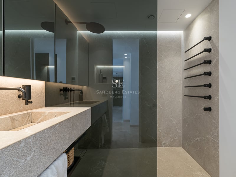 Salle de bain moderne avec lavabo en pierre, robinetterie noir mat et murs en pierre avec paroi de douche en verre.