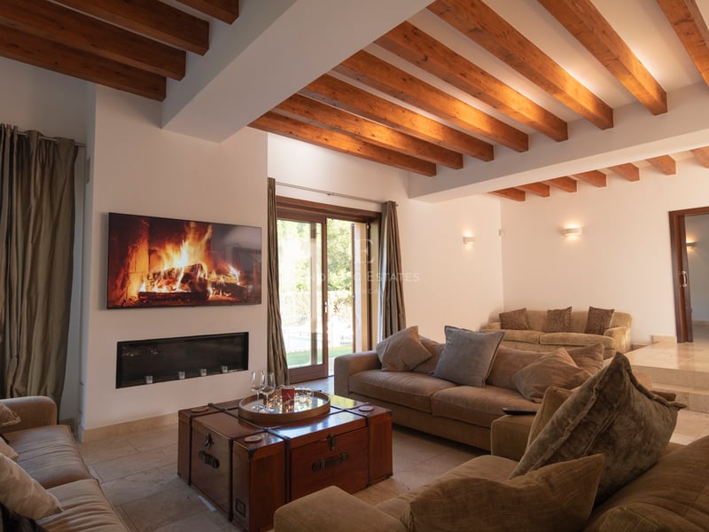 Grand salon avec plafond à poutres en bois, cheminée moderne, sol en pierre et accès direct au jardin.