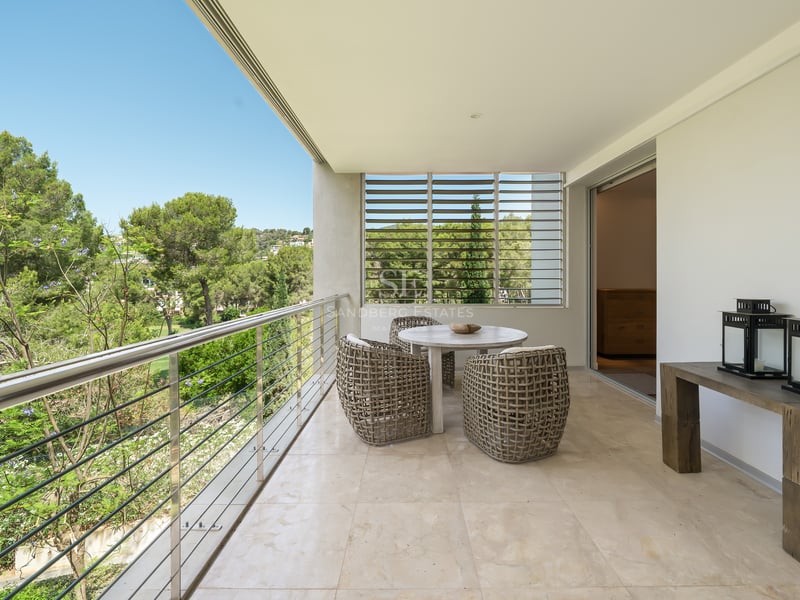 Terrasse spacieuse avec sol en marbre, meubles en osier, garde-corps en acier et vue sur les pins.