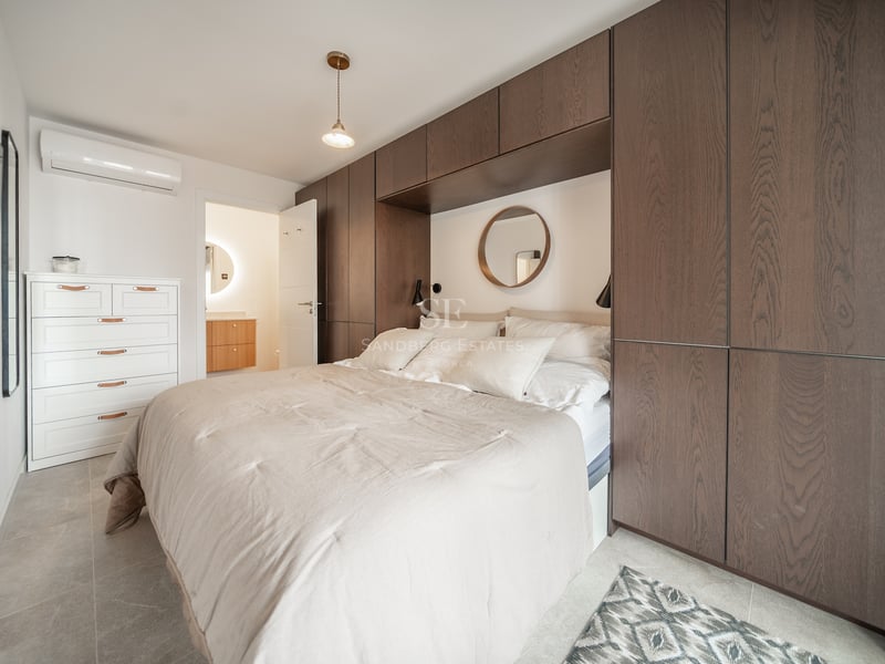 Chambre avec lit double, tête de lit encastrée dans des armoires en bois sombre et miroir rond décoratif.