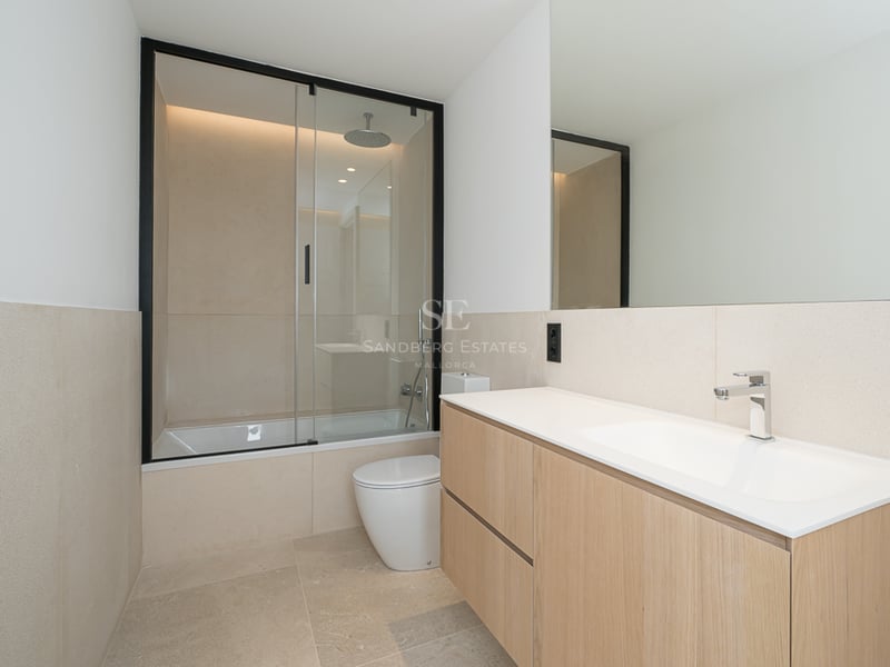 Salle de bain moderne avec meuble en chêne, carrelage en pierre et baignoire avec paroi vitrée noire.