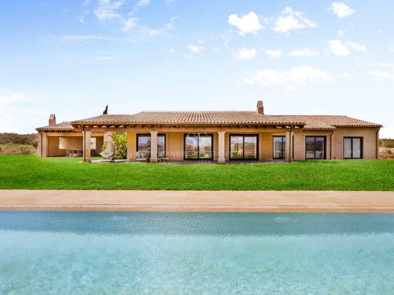 Grande piscine turquoise devant une villa méditerranéenne avec pelouse verte et toit en terre cuite.