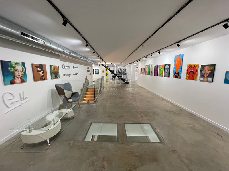 Longue galerie industrielle avec sols en béton poli, murs blancs ornés d'art pop et dalles de verre au sol.