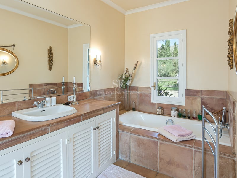 Bright bathroom featuring terracotta tile surfaces, white louvered vanity, built-in bathtub, and large decorative mirrors.
