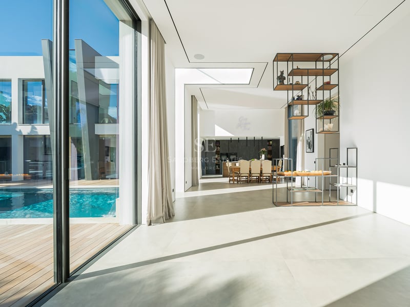 Salon lumineux à aire ouverte avec sols blancs, baies vitrées et vue sur une piscine privée.