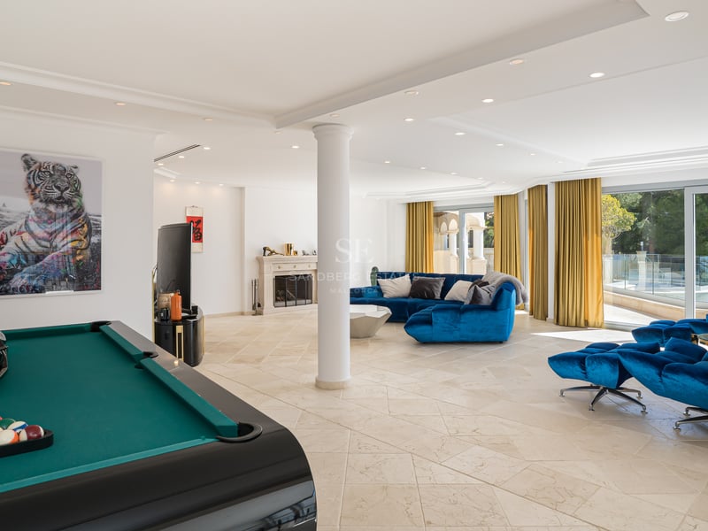 Grande salle de jeux moderne avec canapé bleu, table de billard, sol en pierre et cheminée classique.