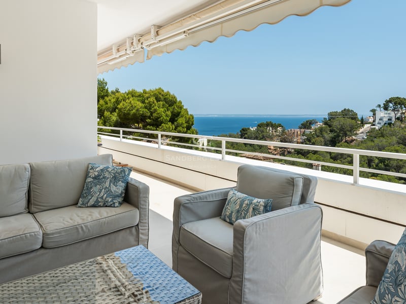 Terrasse couverte avec salon de jardin gris et table en rotin donnant sur la mer et les collines verdoyantes.