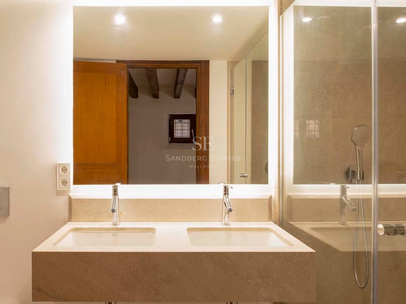 Salle de bain avec double vasque en pierre, grand miroir rétroéclairé et paroi de douche en verre.