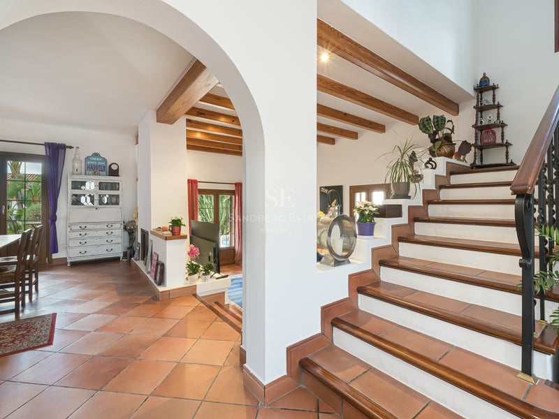Vue intérieure avec sols en terre cuite, arche, poutres en bois au plafond et escalier en fer forgé.
