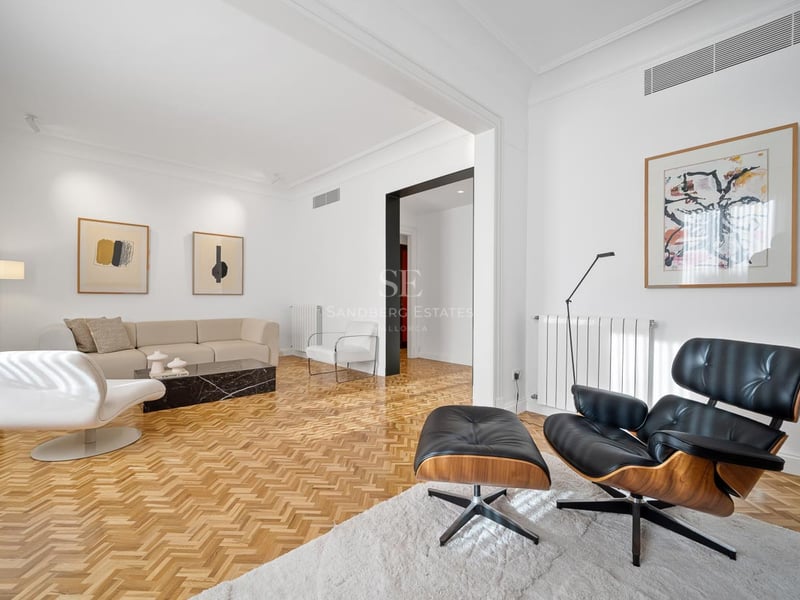 Salon lumineux avec canapé beige, fauteuil Eames noir, table en marbre noir et parquet en chevrons.