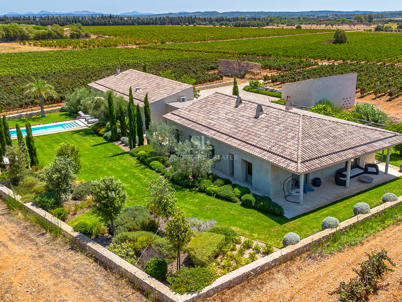 Vue aérienne d'une villa contemporaine avec toits de tuiles, piscine et jardins au milieu de vastes vignobles.