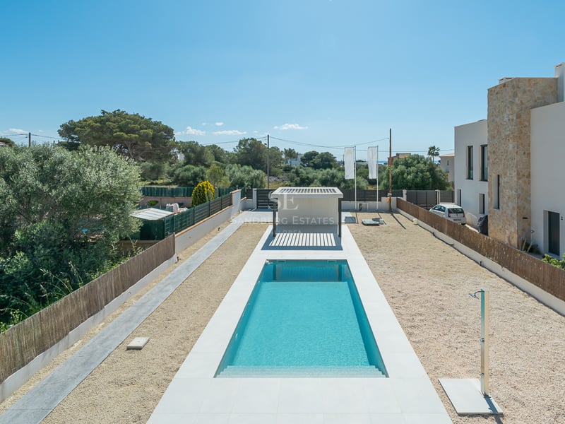 Une longue piscine rectangulaire aux eaux turquoise, entourée de dalles blanches, de gravier et d'une villa contemporaine.