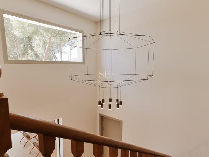 Rampe d'escalier en bois sur un hall double hauteur avec un lustre géométrique moderne et fenêtre haute.
