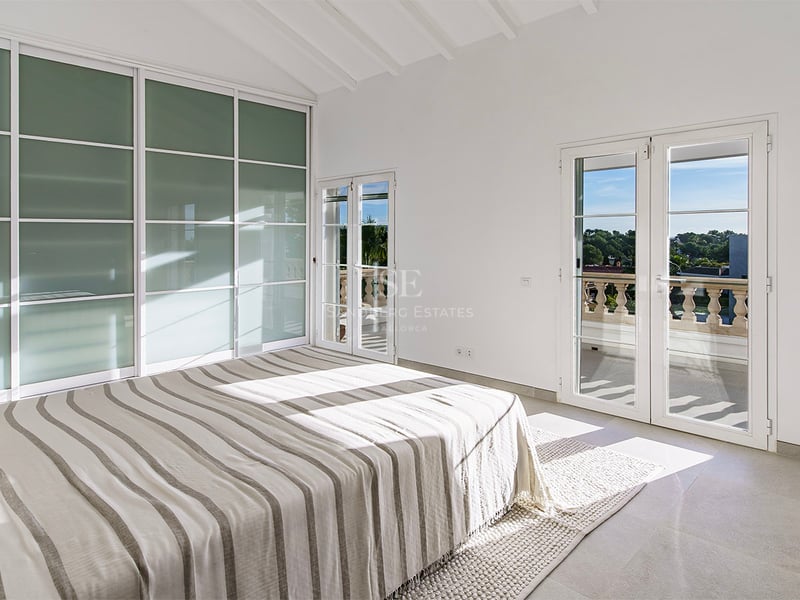 Chambre lumineuse avec lit rayé, plafonds voûtés blancs, placards en verre dépoli et accès à un balcon.