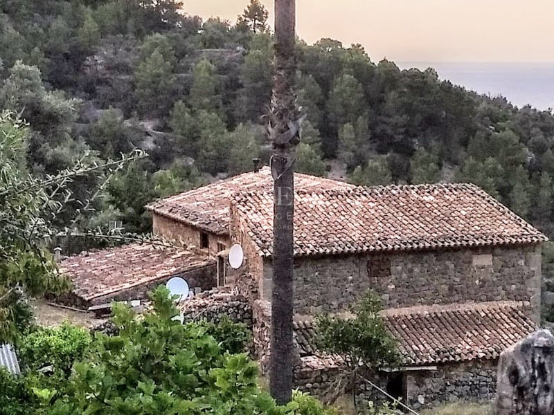 Maison traditionnelle en pierre avec toits en tuiles nichée dans une colline verdoyante surplombant la mer.