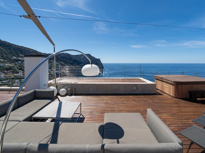 Toit-terrasse moderne avec canapé gris, terrasse en bois et jacuzzi surplombant la mer Méditerranée et les montagnes.
