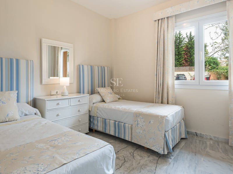 Chambre avec deux lits jumeaux, linge bleu et blanc, commode blanche et sol en marbre poli.