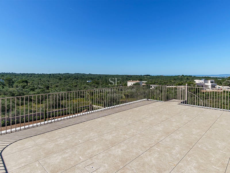 Terrasse en pierre avec garde-corps métallique surplombant un paysage verdoyant sous un ciel bleu azur.