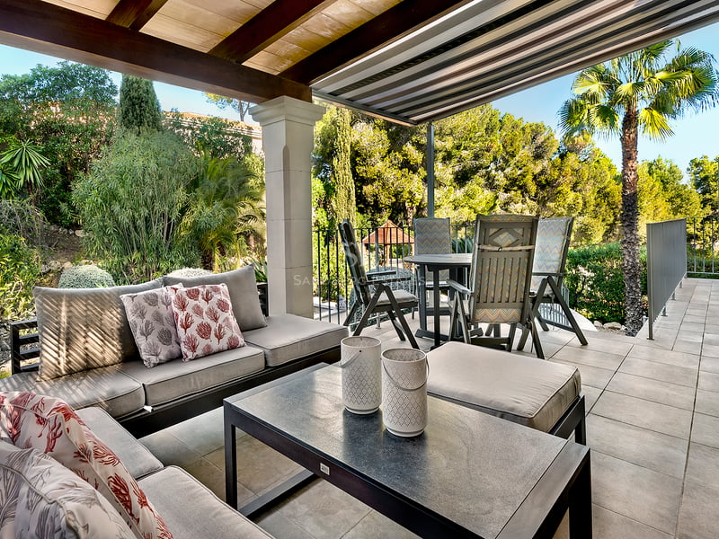 Terrasse extérieure couverte avec canapés, table à manger et vue sur un jardin méditerranéen luxuriant.
