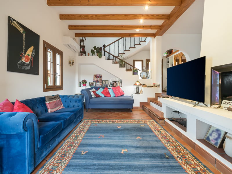 Salon spacieux avec canapés en velours bleu, poutres en bois apparentes au plafond et sol en terre cuite traditionnelle.