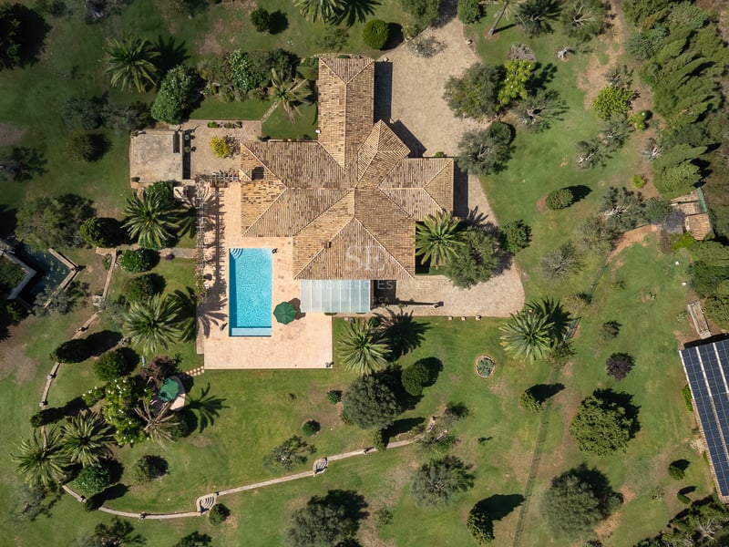Birds-eye aerial view of a large Mediterranean villa featuring a swimming pool, expansive gardens, and solar array.