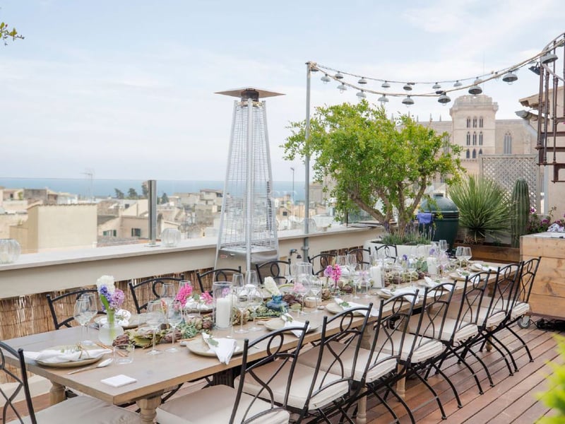 Una mesa de comedor elegantemente decorada en una terraza de madera con vistas a una ciudad histórica y al mar.