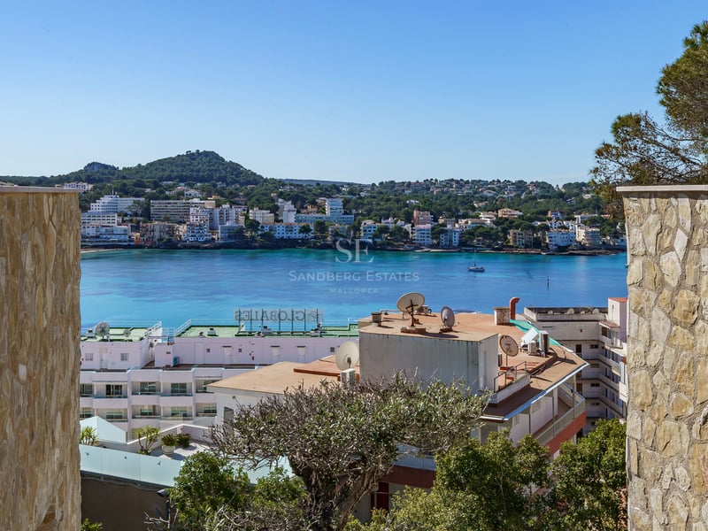 Vue d'une baie méditerranéenne turquoise encadrée par des murs en pierre naturelle sous un ciel bleu clair.