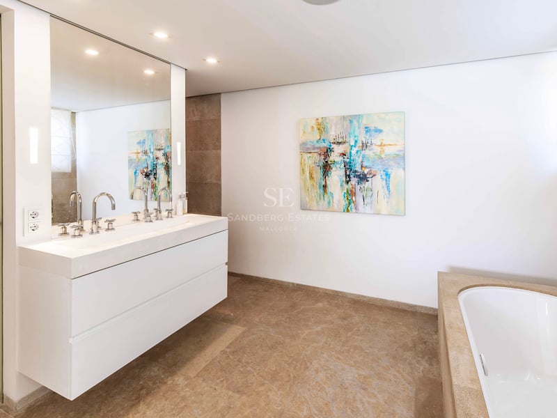 Grande salle de bain principale avec double vasque suspendue blanche, grand miroir et baignoire encastrée en pierre.