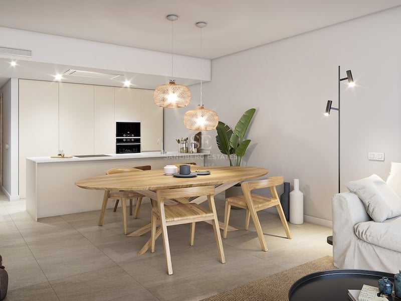Salle à manger moderne avec table ovale en bois, suspensions en osier et cuisine blanche intégrée.