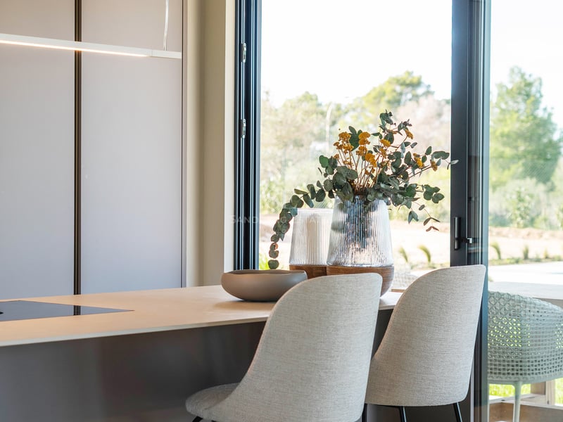 Moderne Kücheninsel mit grauen Barhockern neben einer großen Glastür mit Blick in den Garten.