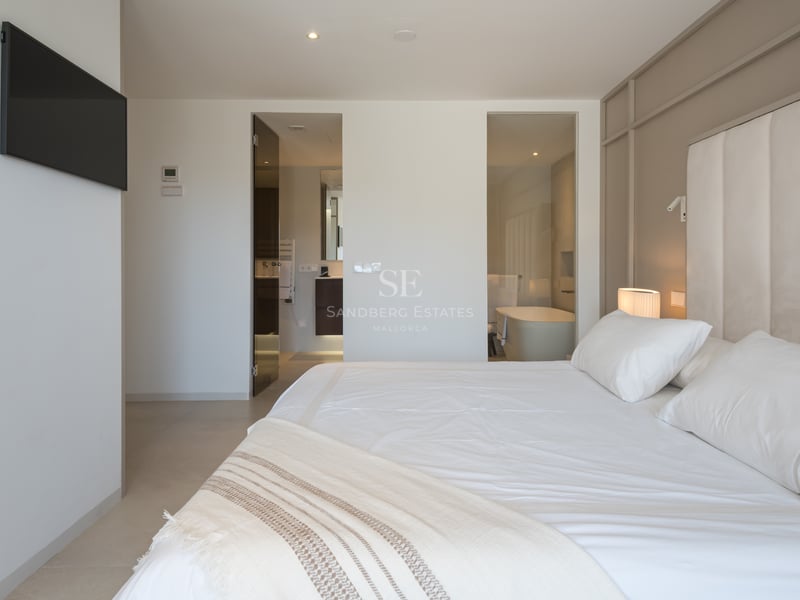 Chambre de maître moderne avec grand lit, tête de lit rembourrée et vue sur la salle de bain privative.