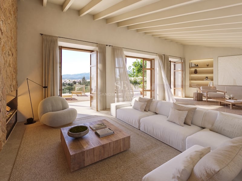 Salon lumineux avec canapé blanc, cheminée en pierre, poutres en bois et portes ouvrant sur une terrasse ensoleillée.