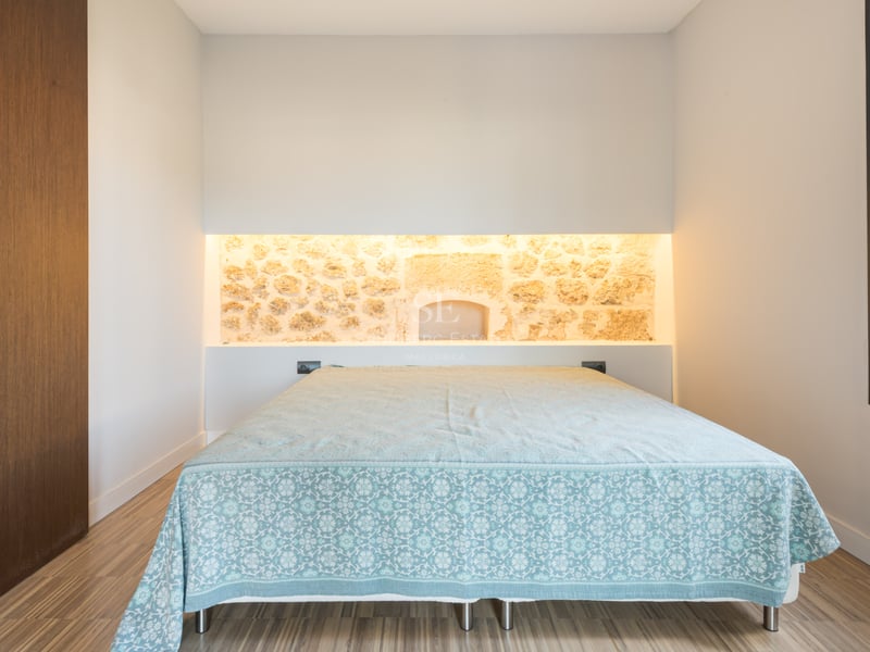 Chambre à coucher avec un lit, un mur en pierre éclairé par l'arrière et du parquet au sol.